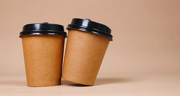 two coffee cups with blank branding next to one another on a brown background