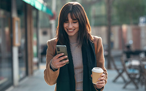 a woman using her mobile phone in one hand and a coffee cup in another hand 