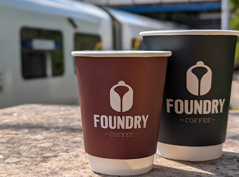 two coffee cups branded with Foundry coffee at a train station