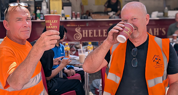 two men in hi-vis jackets holding coffee cups with Shelley & Sarah's branding on them