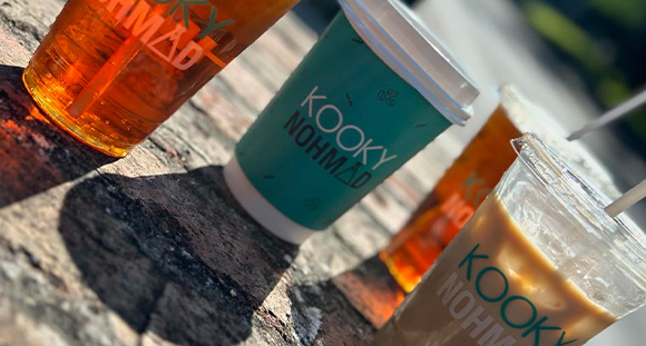 four coffee cups on a pavement with Kooky Nohmad branded on the front