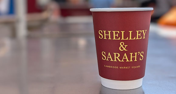 a red coffee cup branded Shelley and Sarah's on a grey indoor floor