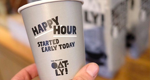 a person holding a branded coffee cup in front of Oatly milk cartons