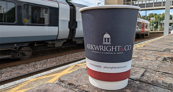 a branded coffee cup sitting on the ground with a train station in the background